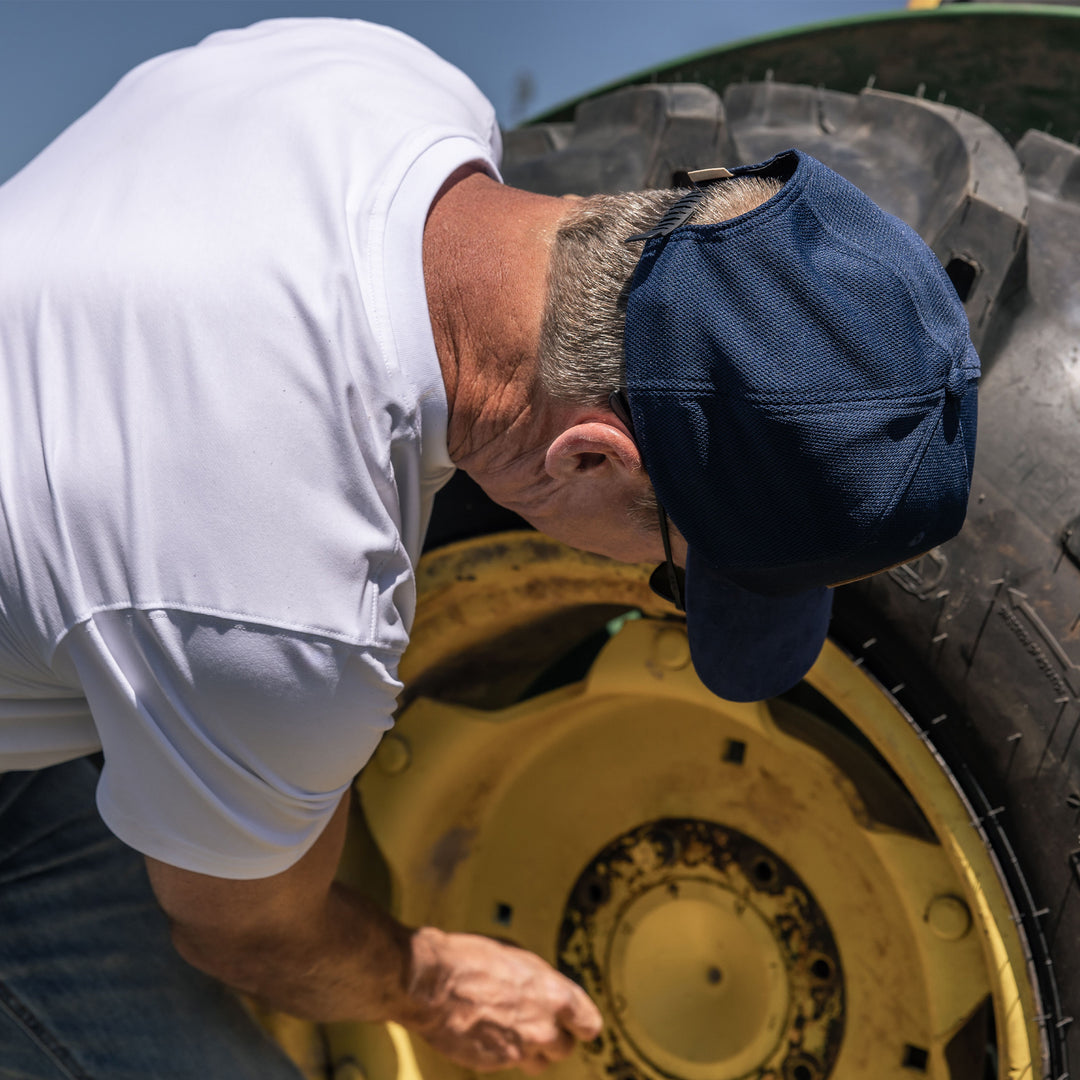 Man wearing a blue mesh trucker cap while working on a tractor #color_blue